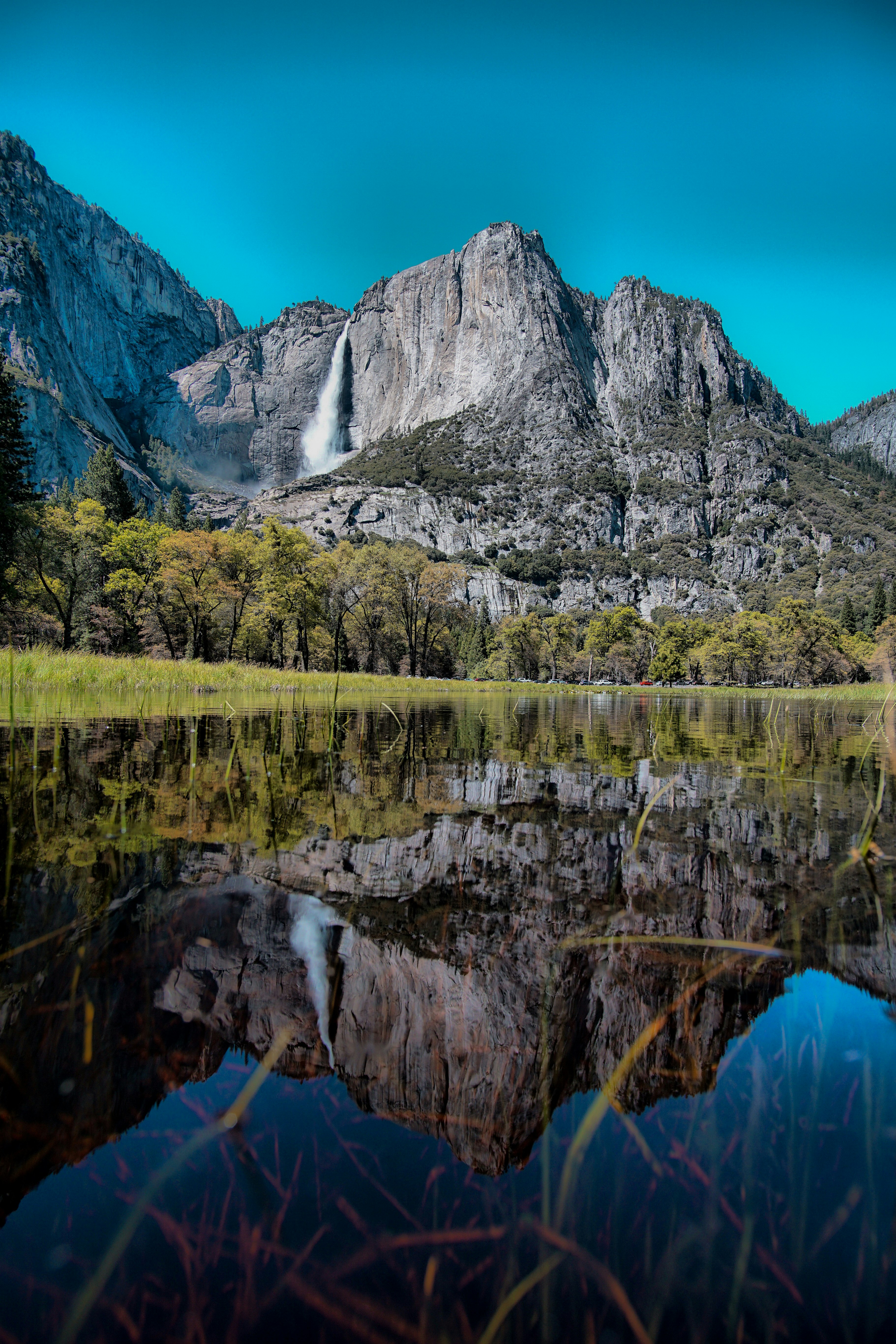 calm body of water overlooking waterfalls and gray rock mountain under blue sky at daytime